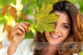 wdnetstudio Portrait of a beautiful and lovely young woman holding fallen leaf and smiling in the park on a sunny day.