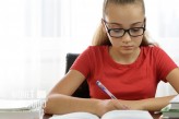 wdnetstudio                             Beautiful girl is writing a homework or doing a notes in a notebook on a desk full of books.            