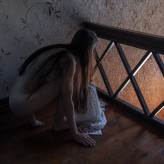 piotrwisinski Naga, skryta w półcieniu – jakby chciała się ukryć, a jednak spogląda. Zawstydzona, ale obecna. Jej ciało ledwie muśnięte żółtym światłem, które wpada przez otwarte drzwi, niewidoczne w kadrze. Intymna chwila pomiędzy chęcią bycia