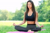 wdnetstudio Attractive and young woman doing yoga meditation in a lotus pose outdoors in a park on a sunny day