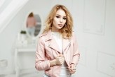 Alonesdj Beautiful blonde woman with curly hair in a fashionable pink leather jacket standing in the room